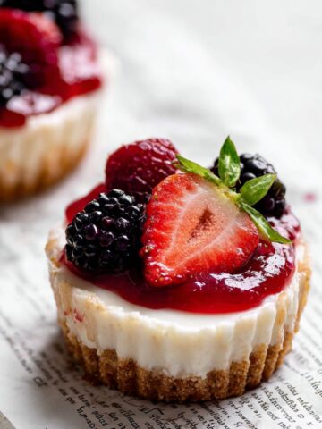 Easy Mini No-Bake Cheesecakes Recipe 1 Mini No-Bake Cheesecakes with graham cracker crust, topped with mixed fresh berries and berry sauce, served on parchment paper.