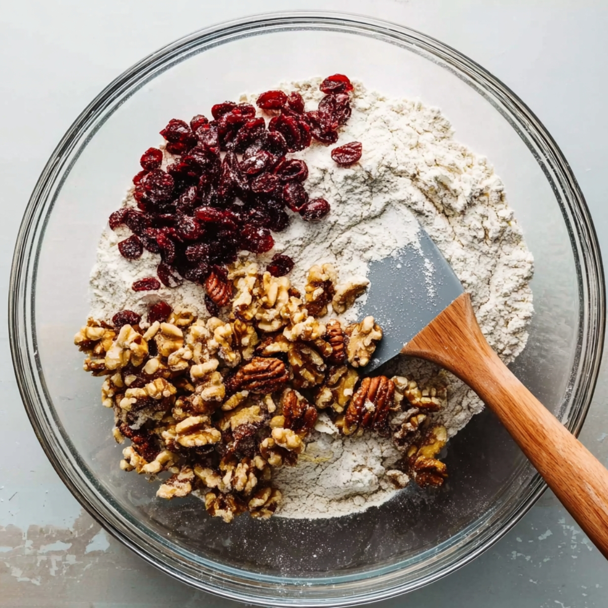 Cranberry Nut No-Knead Bread Recipe 10 Dry ingredients for cranberry walnut bread, including flour, cranberries, and walnuts, being mixed in a glass bowl.