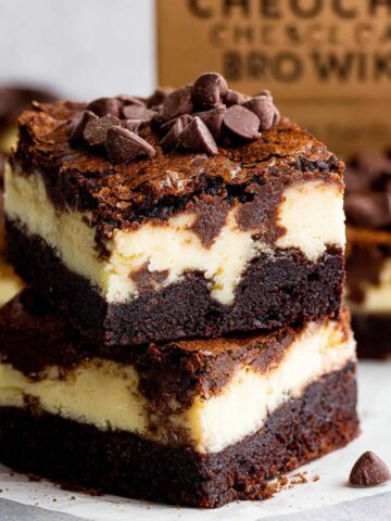 Two Mocha Cheesecake Brownies stacked on top of each other, with a visible cheesecake layer in the center, topped with chocolate chips, and showing the rich layers of brownie and cheesecake.