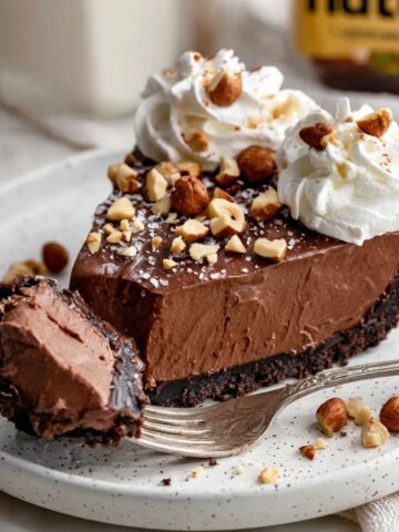 The Best Nutella Cream Pie Recipe 2 A slice of Nutella Cream Pie topped with whipped cream swirls, crushed hazelnuts, and a sprinkle of sea salt.
