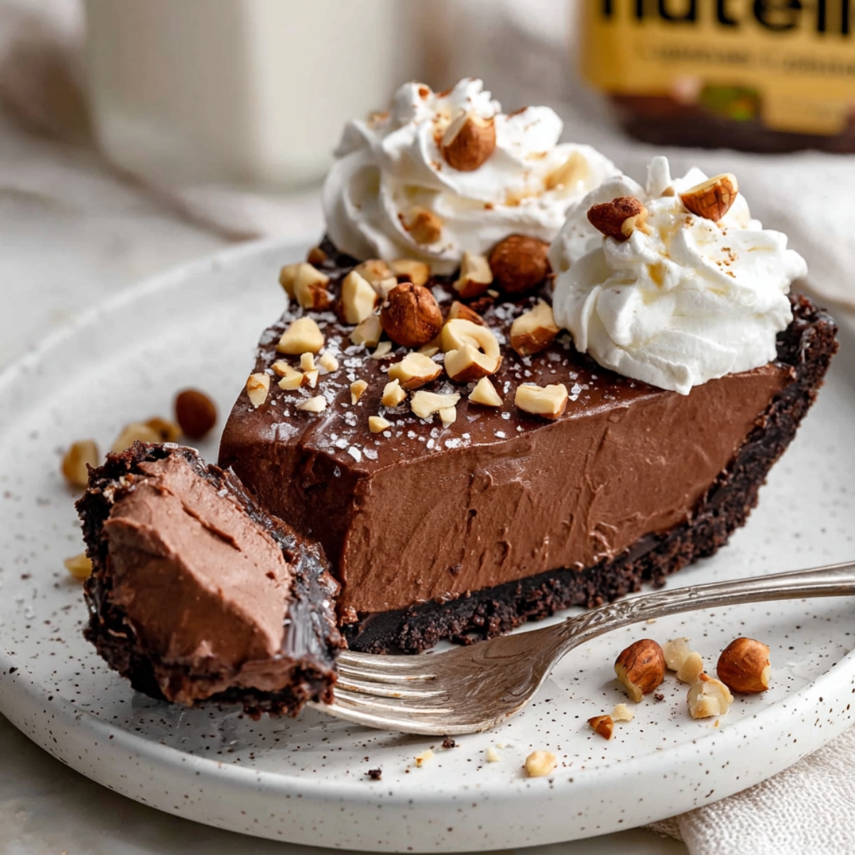 A slice of Nutella Cream Pie topped with whipped cream swirls, crushed hazelnuts, and a sprinkle of sea salt.
