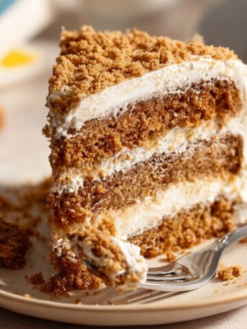 Easy Oatmeal Cream Pie Cake Recipe 1 A slice of Oatmeal Cream Pie Cake on a plate, layered with creamy frosting and topped with crumbled oatmeal cookies, with a fork taking a bite.