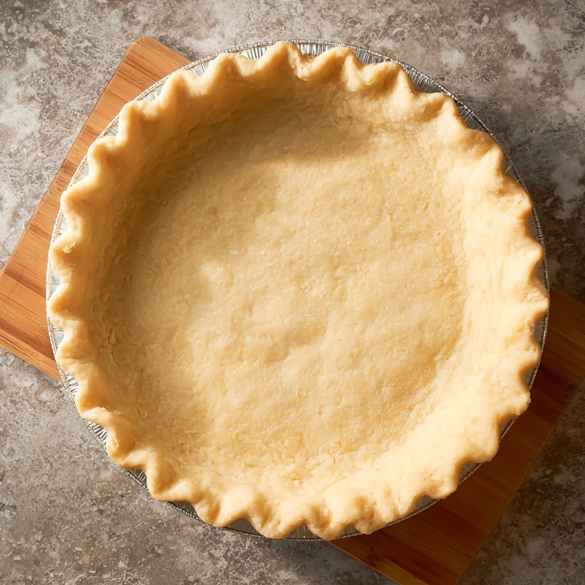 The Best Orange Pie Recipe 10 Unbaked homemade pie crust with fluted edges in an aluminum pie tin resting on a wooden board over a marble surface.