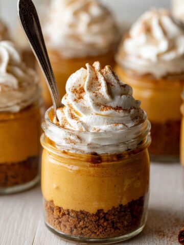 Easy Pumpkin Pie in a Jar Recipe 2 Individual Pumpkin Pie in a Jar with a Biscoff cookie crust, topped with creamy pumpkin filling and swirls of whipped cream sprinkled with cinnamon, perfect fall dessert presentation.