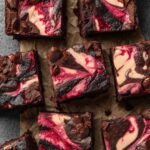 Fudgy Raspberry Cheesecake Brownies cut into squares with vibrant pink cheesecake swirls and chocolate chunks on parchment paper.