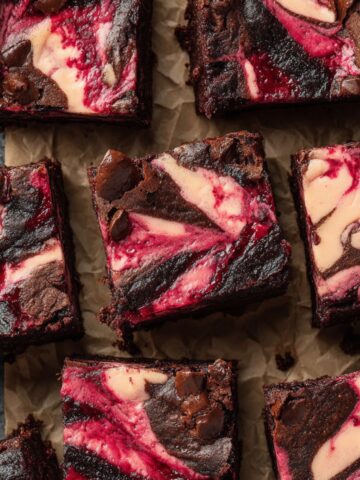 Raspberry Cheesecake Brownies Recipe 2 Fudgy Raspberry Cheesecake Brownies cut into squares with vibrant pink cheesecake swirls and chocolate chunks on parchment paper.