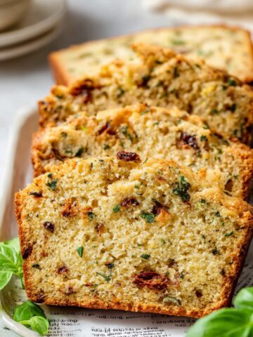 Easy Savory Quick Bread Recipe 2 Slices of baked Savory Quick Bread with herbs and sun-dried tomatoes on a plate.