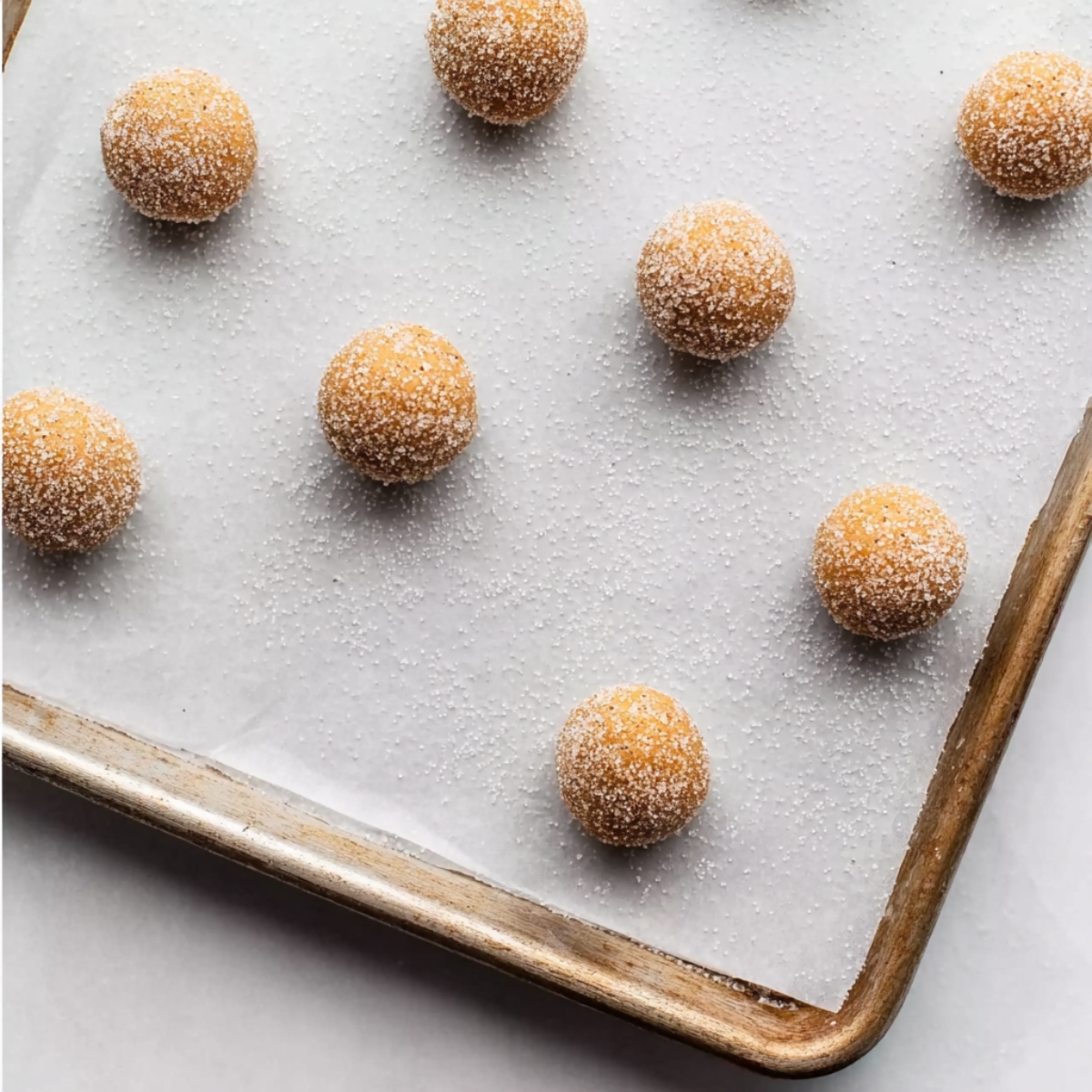 The Best Gingerbread Blossoms Recipe 11 Sugar-coated gingerbread cookie dough balls evenly spaced on a parchment-lined baking sheet, ready to be baked.