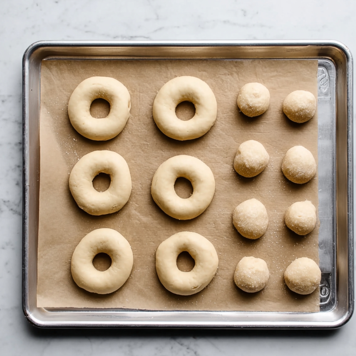 Homemade Glazed Doughnuts Recipe 11 Uncooked doughnuts and dough balls neatly arranged on a parchment-lined baking sheet, ready for baking, showing smooth, round dough texture.