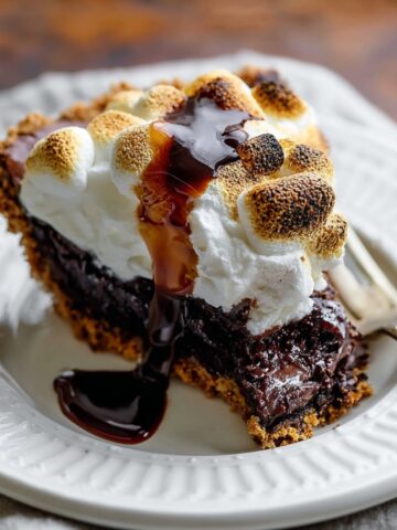 Easy S'mores Brownie Pie Recipe 2 Slice of S'mores Brownie Pie topped with toasted marshmallows and chocolate sauce on a white dessert plate.