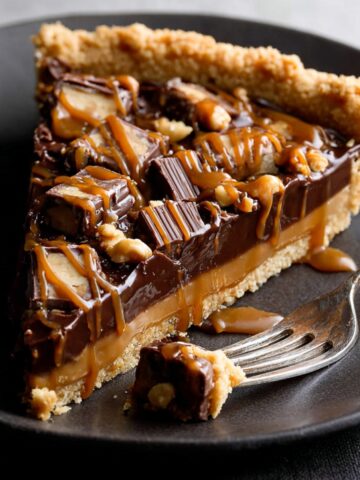 Easy Snickers Caramel Tart Recipe 2 Slice of Snickers Caramel Tart on a black plate, fork cutting a piece
