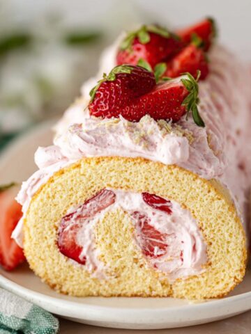 Easy Strawberry Cake Roll Recipe 1 Slice of Strawberry Cake Roll filled with whipped strawberry cream, decorated with fresh strawberries on top, served on a plate.