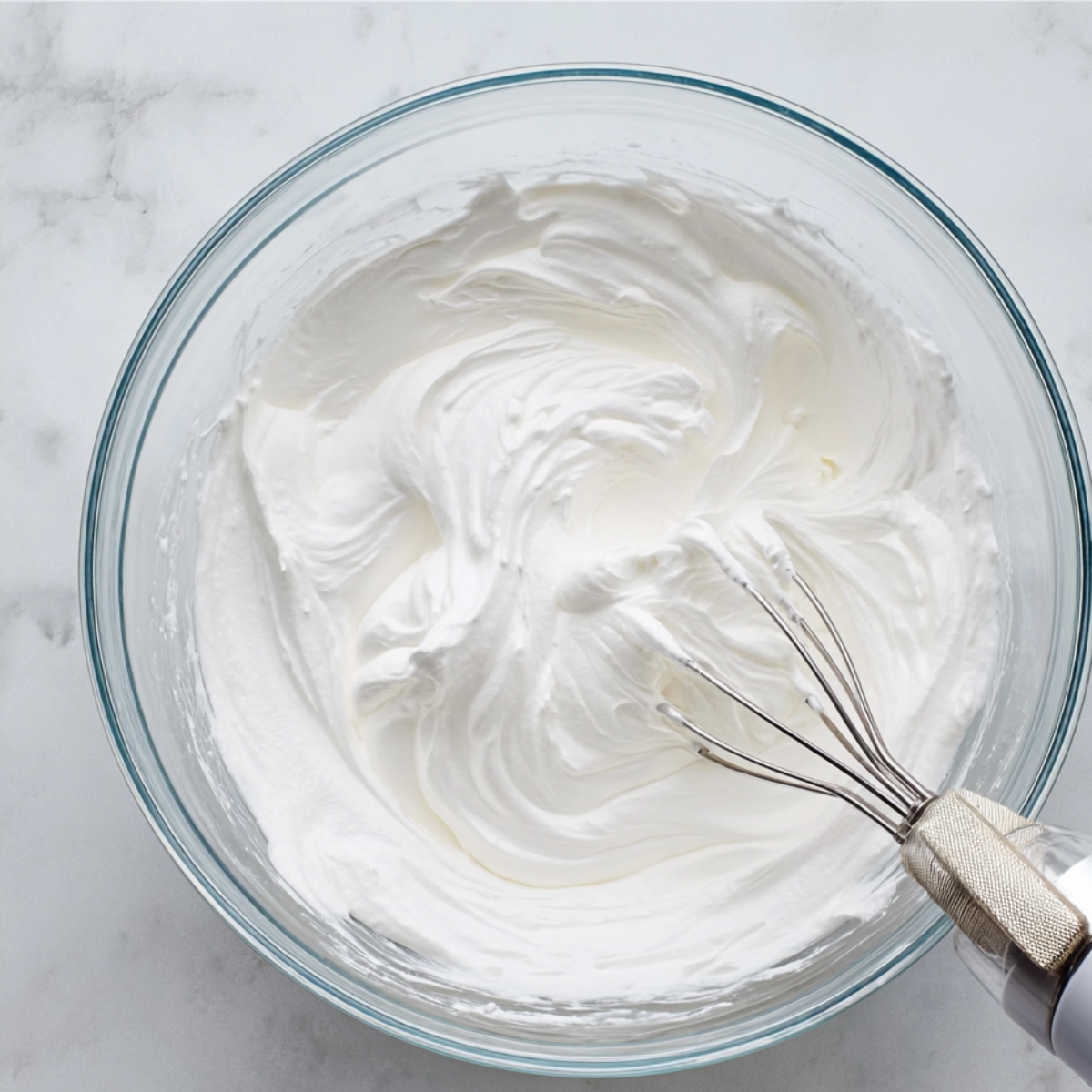 Easy Mini Lemon Meringue Tarts 11 A glass mixing bowl filled with fluffy, stiff peaks of whipped meringue, with a hand mixer resting inside.
