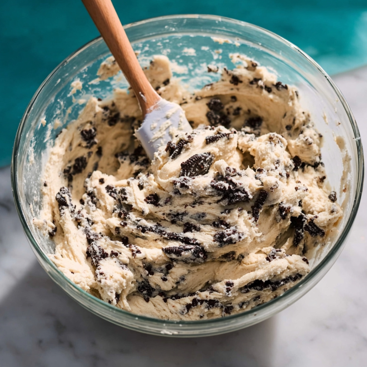 Easy Cookies and Cream Cookies 10 Thick cookies and cream cookie dough mixed with crushed chocolate sandwich cookies in a clear glass bowl with a spatula, ready to be scooped and baked.