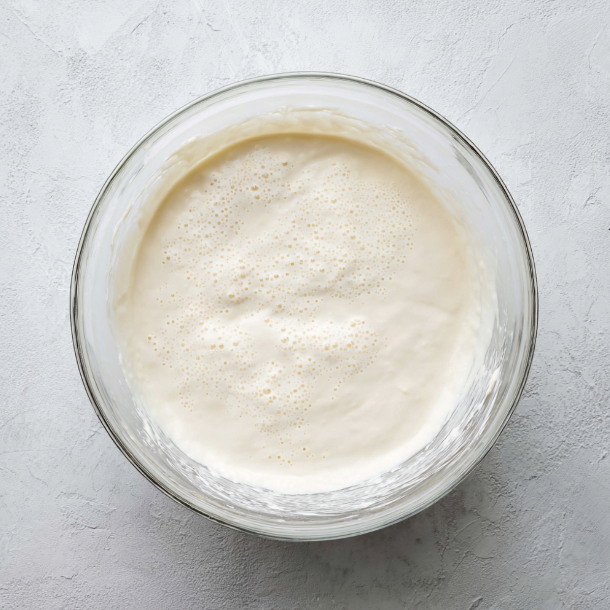 Easy Marshmallow Brownies Recipe 10 Top-down shot of whipped marshmallow mixture in a glass bowl on a light textured background, smooth and airy with tiny bubbles, prepared for swirling into brownie batter.