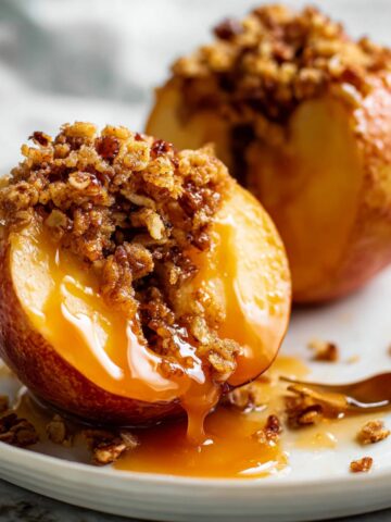 Easy Homemade Baked Apples Recipe 2 Close-up of warm Baked Apples filled with a crunchy oat and pecan crumble topping, drizzled with rich caramel sauce and served on a white plate for a cozy fall dessert.