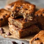 Stacked Banana Bars with Chocolate Chips with a bite taken from the top square, showcasing a soft, moist crumb and melted chocolate chips.