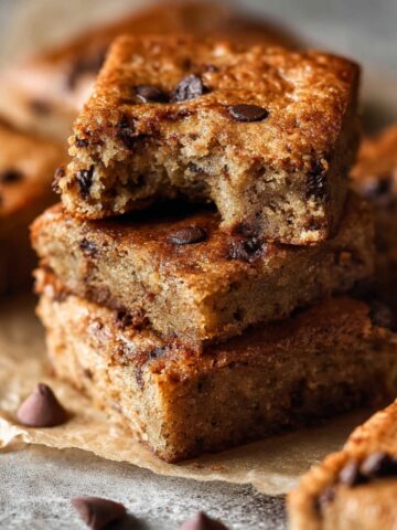 Easy Banana Bars with Chocolate Chips 2 Stacked Banana Bars with Chocolate Chips with a bite taken from the top square, showcasing a soft, moist crumb and melted chocolate chips.