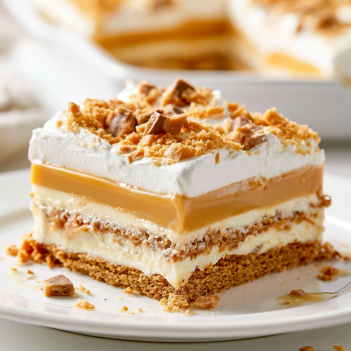 The Best Butterscotch Lush Recipe 9 Slice of Butterscotch Lush dessert on a white plate featuring layers of graham cracker crust, cream cheese filling, butterscotch pudding, and whipped topping, finished with crushed toffee pieces.