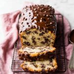 Chocolate Chip Loaf Cake topped with glossy chocolate glaze and mini chocolate chips, sliced and served on a cooling rack with a pink linen cloth.