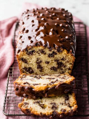 Chocolate Chip Loaf Cake Recipe 1 Chocolate Chip Loaf Cake topped with glossy chocolate glaze and mini chocolate chips, sliced and served on a cooling rack with a pink linen cloth.