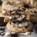 Easy Cookies and Cream Cookies 12 Soft-baked Cookies and Cream Cookies stacked on parchment paper, showing a chewy center filled with crushed Oreo cookies and white chocolate chips.