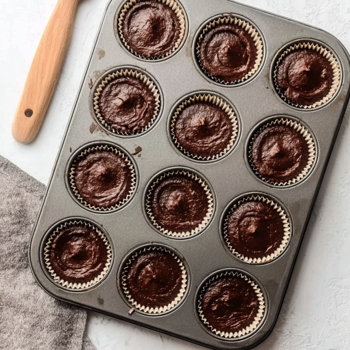The Best Snickers Cupcakes Recipe 11 Chocolate cupcake batter evenly filled into paper liners inside a nonstick muffin tray, top view baking preparation scene with rich dark chocolate texture and cozy homemade dessert aesthetic.