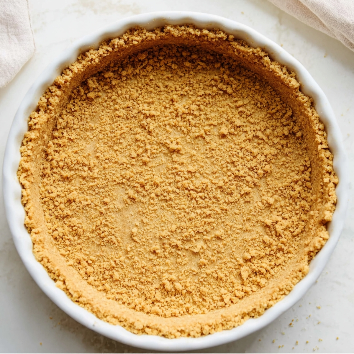 No-Bake Banana Cream Cheesecake 10 Homemade graham cracker pie crust pressed into a white fluted pie dish, showing an even golden crumb texture before filling.