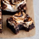 Close-up of a fudgy Marshmallow Brownies with a bite taken out, featuring toasted marshmallow swirls and rich chocolate marbling on parchment paper.