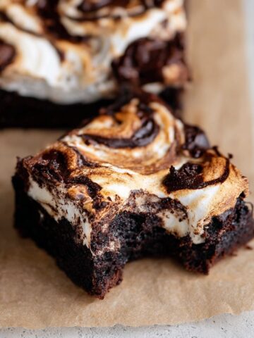 Easy Marshmallow Brownies Recipe 1 Close-up of a fudgy Marshmallow Brownies with a bite taken out, featuring toasted marshmallow swirls and rich chocolate marbling on parchment paper.