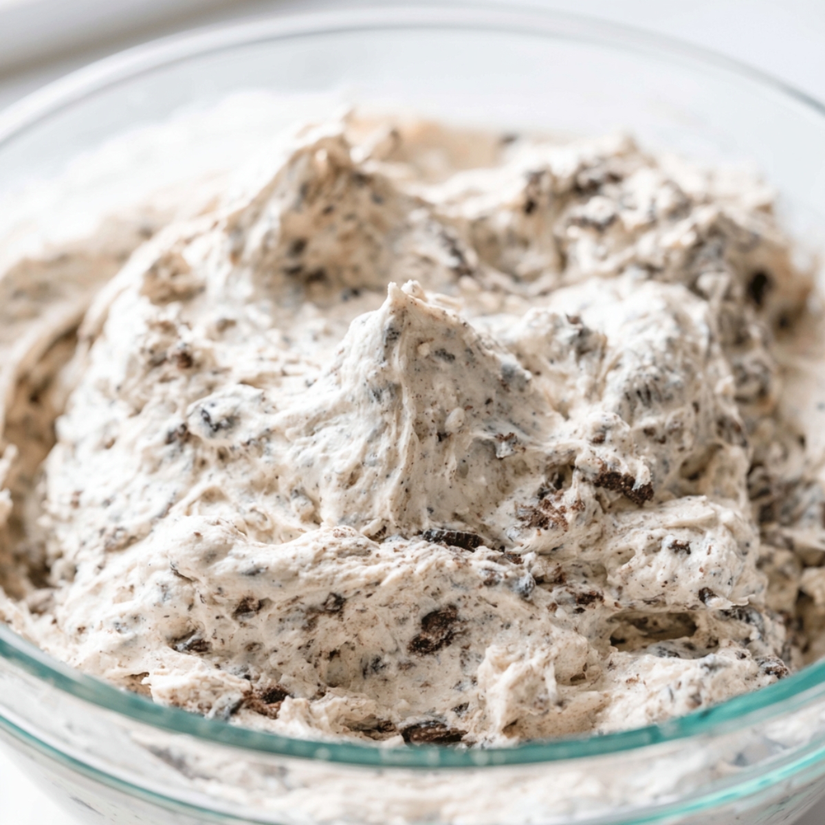Easy Oreo Pudding Pie Recipe 10 Close-up of thick cookies-and-cream pie filling in a glass mixing bowl, showing fluffy whipped texture with crushed Oreo cookie pieces throughout.