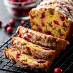 Slices of Orange Glazed Cranberry Bread with streusel topping arranged on a cooling rack, showcasing a moist crumb filled with cranberries and pumpkin seeds.
