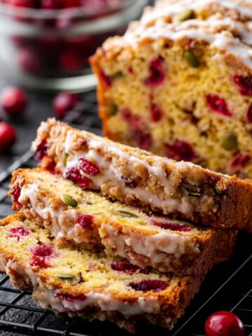 Easy Orange Glazed Cranberry Bread 1 Slices of Orange Glazed Cranberry Bread with streusel topping arranged on a cooling rack, showcasing a moist crumb filled with cranberries and pumpkin seeds.