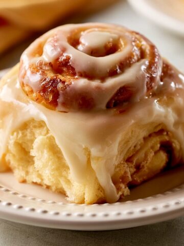 Homemade Orange Sweet Rolls Recipe 2 Freshly baked Orange Sweet Roll topped with creamy glaze, served on a white decorative plate, showcasing fluffy layers and rich icing dripping over the sides.