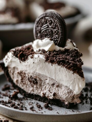 Easy Oreo Pudding Pie Recipe 1 Slice of Oreo Pudding Pie topped with whipped cream, Oreo cookie crumbs, and a whole Oreo cookie garnish on a gray dessert plate, with a chocolate cookie crust and creamy cookies-and-cream filling.