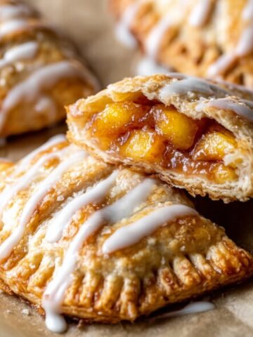 Easy Peach Hand Pies Recipe 2 Golden-brown Peach Hand Pies drizzled with vanilla glaze, featuring flaky pastry and juicy peach filling, perfect for a homemade summer dessert.
