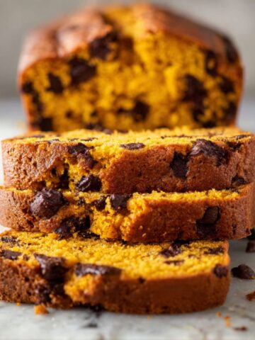 Pumpkin Chocolate Chip Bread Recipe 1 Freshly baked Pumpkin Chocolate Chip Bread sliced on a marble countertop, showing a moist orange crumb studded with melted chocolate chips.