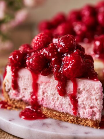 Easy Raspberry Cheesecake Recipe 1 Slice of raspberry cheesecake topped with fresh raspberry compote, featuring a creamy pink filling, graham cracker crust, and vibrant berry sauce dripping down the sides.