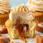 Close-up of a Salted Caramel Cupcakes cut in half, revealing a rich gooey caramel filling, topped with swirled caramel buttercream and caramel candy pieces.