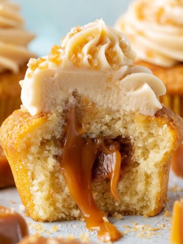 Easy Salted Caramel Cupcakes Recipe 2 Close-up of a Salted Caramel Cupcakes cut in half, revealing a rich gooey caramel filling, topped with swirled caramel buttercream and caramel candy pieces.