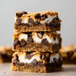 Stacked S'mores Cookie Bars with gooey marshmallow filling, melted chocolate chips, and golden graham cookie layers, close-up dessert photography showcasing rich texture and indulgent homemade treats.