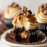 Decadent Snickers Cupcakes with creamy peanut butter frosting, caramel drizzle, chopped chocolate candy topping, and gooey peanut butter center, close-up gourmet dessert photography with soft bakery lighting.