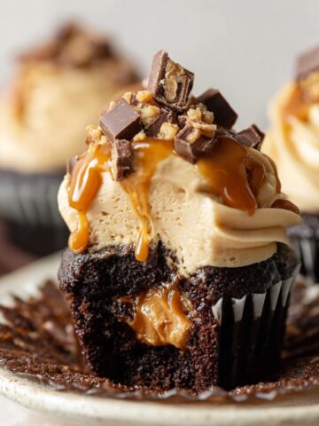 The Best Snickers Cupcakes Recipe 2 Decadent Snickers Cupcakes with creamy peanut butter frosting, caramel drizzle, chopped chocolate candy topping, and gooey peanut butter center, close-up gourmet dessert photography with soft bakery lighting.