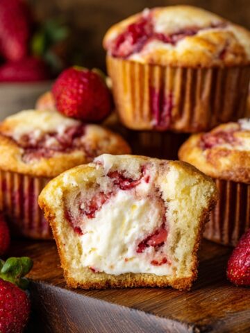 Strawberry Cream Cheese Muffins cut open to reveal a creamy cheesecake filling, surrounded by fresh strawberries and golden baked muffins.