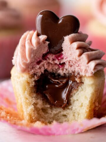 Strawberry Nutella Cupcakes Recipe 1 Strawberry Nutella Cupcakes with pink strawberry buttercream frosting, a chocolate heart topper, and a gooey Nutella-filled center exposed in a bite-sized cross-section.