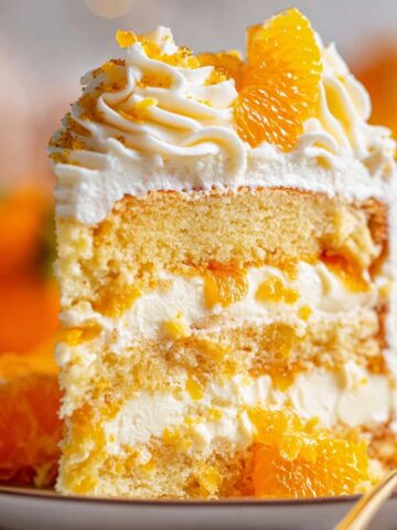 Easy Sunshine Citrus Cake Recipe 1 Tall slice of Sunshine Citrus Cake filled with whipped cream and mandarin oranges, topped with piped frosting and fresh orange segments on a dessert plate.