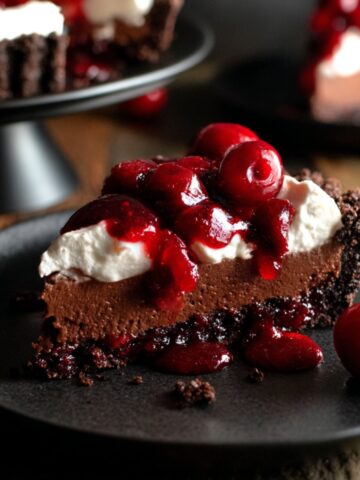 The Best Black Forest Tart Recipe 1 Slice of Black Forest Tart topped with whipped cream and cherry compote on a black dessert plate