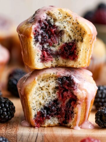 Blackberry Lemon Poppy Seed Muffins 2 Stacked Blackberry Lemon Poppy Seed Muffins with pink lemon glaze and juicy berry-filled centers on a rustic wooden board.