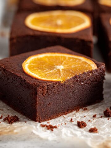 Best Chocolate Orange Brownies Recipe 1 Close-up of fudgy Chocolate Orange Brownies cut into thick squares with baked orange slices on top, served on parchment paper.