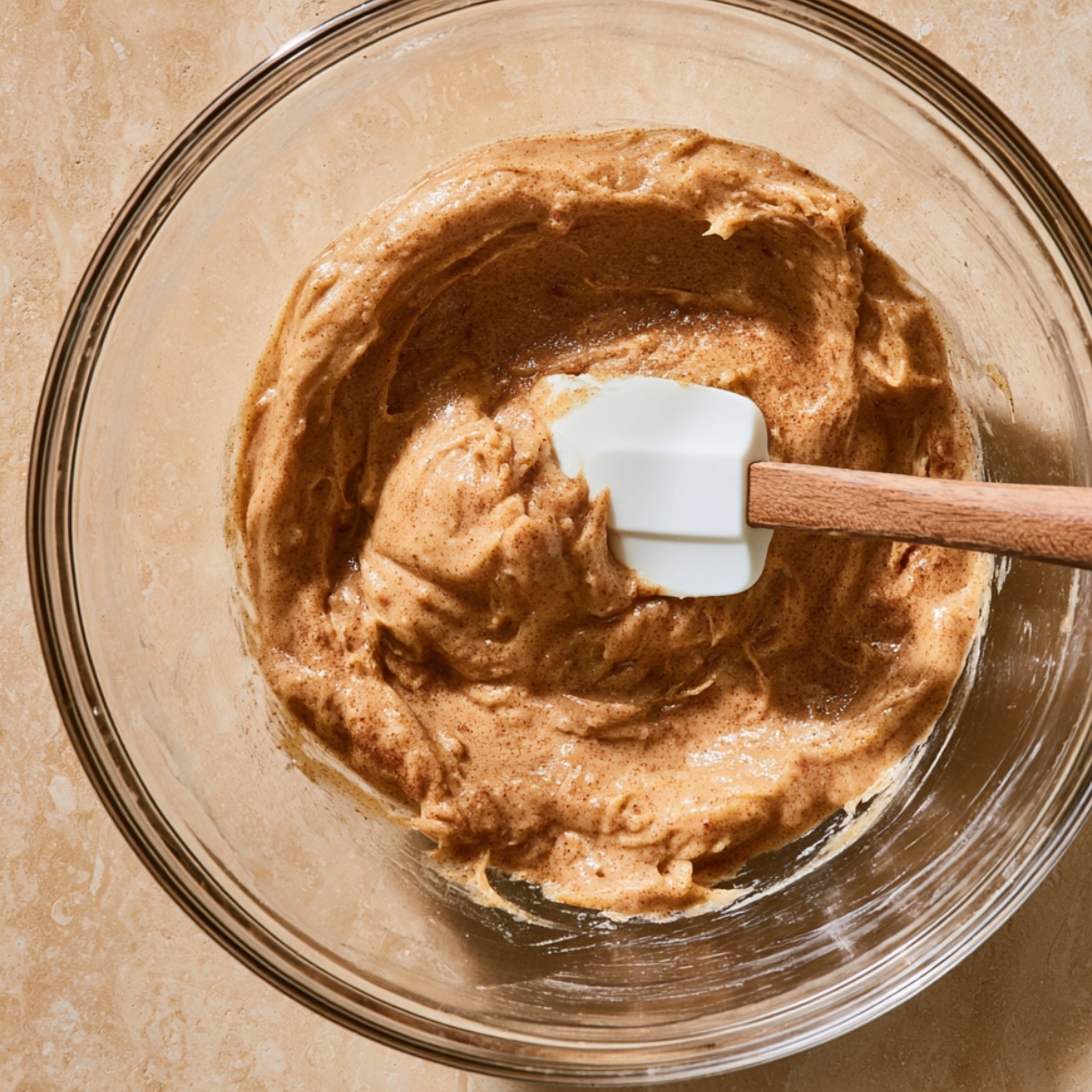 Easy Apple Cider Cookies Recipe 10 Thick cinnamon-spiced apple cider cookie dough being mixed in a clear glass bowl with a white silicone spatula.